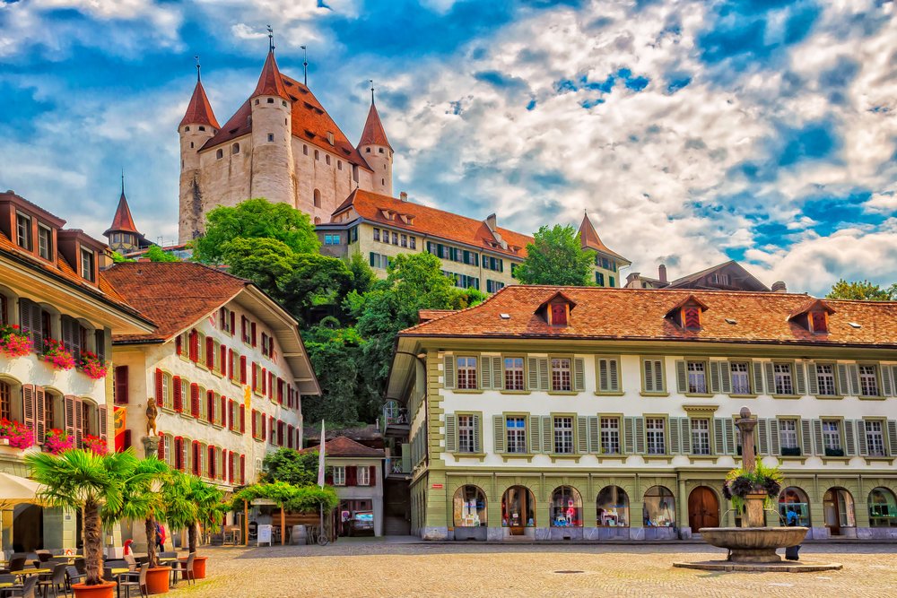 Das Schloss Thun über den ockerfarbenen Häusern der Altstadt, darunter ein Platz mit Brunnen und Bäumen.