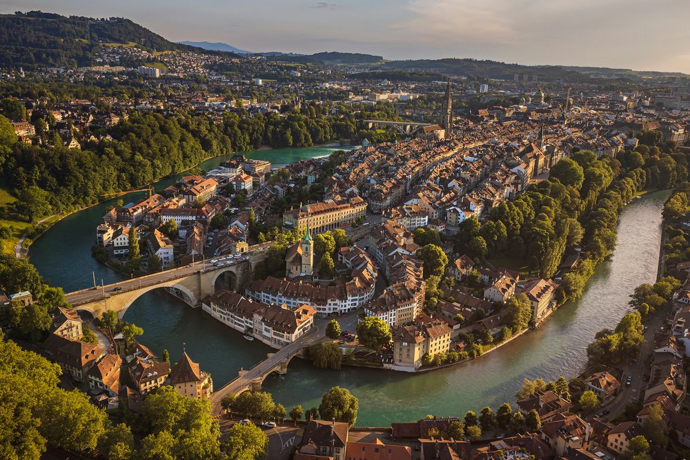 Die Berner Altstadt von oben: die Aare zieht eine enge grüne Schlaufe um die Halbinsel mit ihren Ziegeldächern und Brücken.