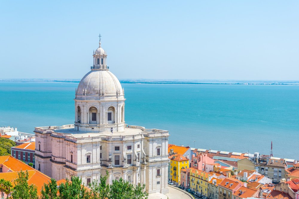 Die weisse Kuppel des Panteão Nacional über den Dächern der Alfama, dahinter der türkisfarbene Tejo bis zum Horizont.