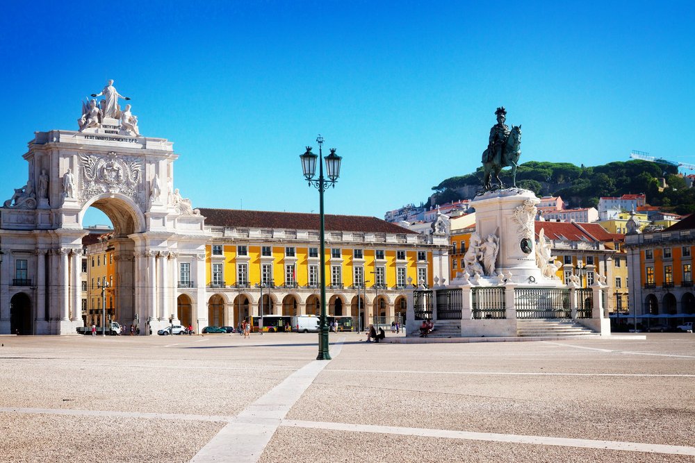 Die Praça do Comércio: ein weiter, flacher Platz am Wasser mit gelben Arkaden, dem Triumphbogen und dem Reiterstandbild.