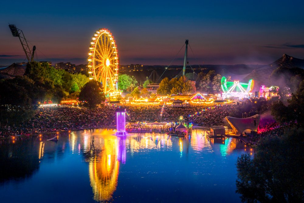 Der Olympiasee bei Nacht: die Lichter eines Sommerfests mit Riesenrad spiegeln sich über die ganze Breite des Wassers.
