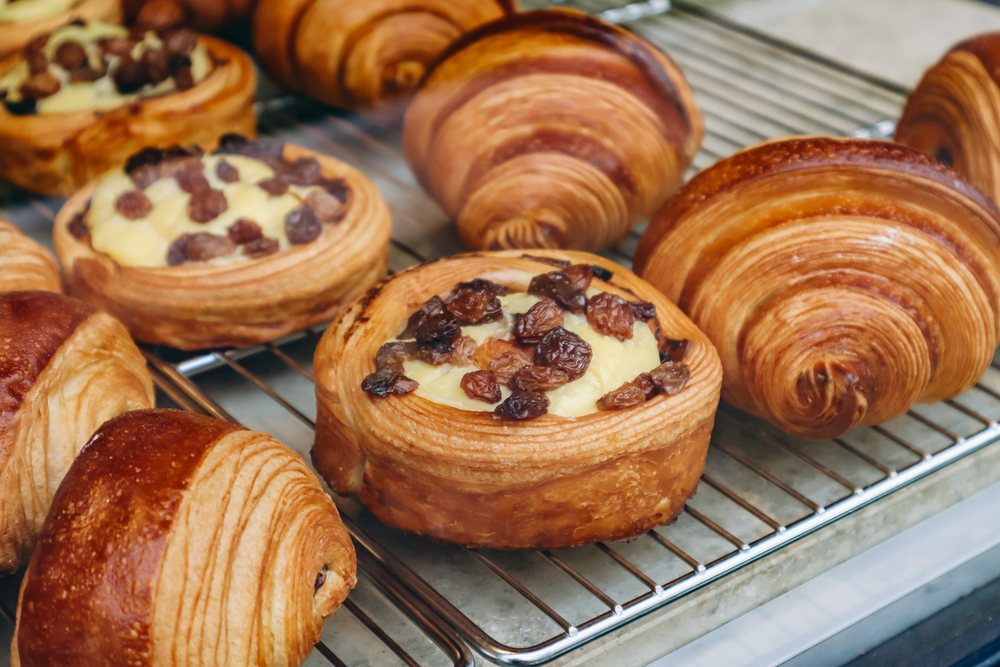 Frisch gebackene Croissants, Pains au chocolat und Rosinenschnecken auf einem Abkühlgitter in einer Bäckerei.