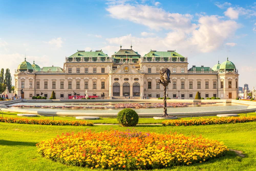 Schloss Belvedere hinter dem Wasserbecken, davor ein Beet aus gelben und orangen Blumen.