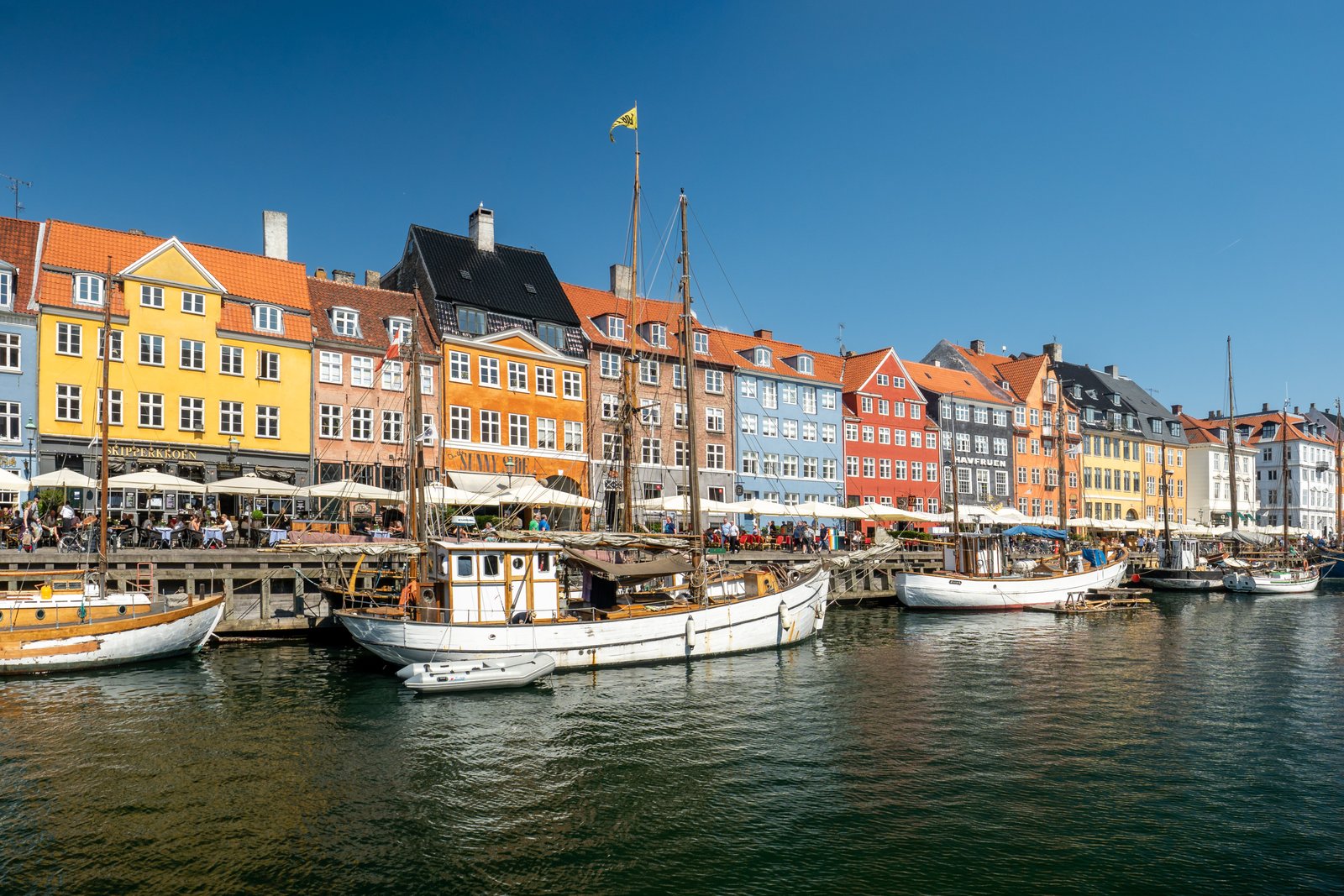 Der Hafen Nyhavn in Kopenhagen: eine Reihe schmaler Häuser in Gelb, Rot und Ocker am Wasser, davor Holzboote und Segelmasten.
