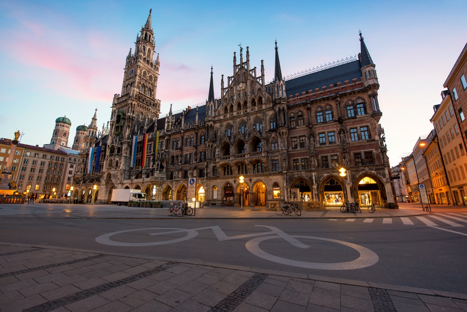 Der Marienplatz in München in der Morgendämmerung: das Neue Rathaus mit seinem Turm über einem leeren, hell gepflasterten Platz, der Himmel geht von Blau in Rosa über.